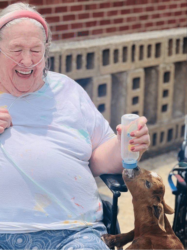 Linley Park resident smiling while feeding a bottle to a baby goat